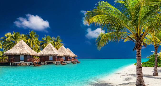 Over water bungalows on a tropical island with palm trees and amazing vibrant beach